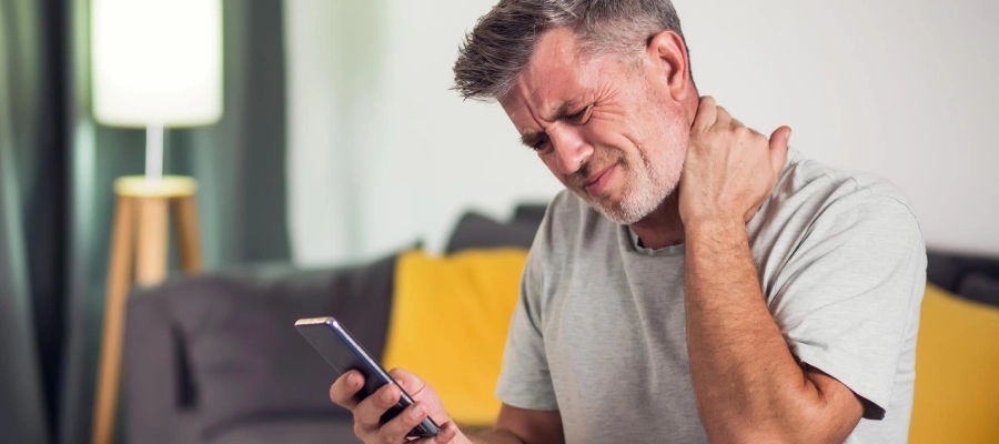 o homem com dor no pescoço e o celular na mão
