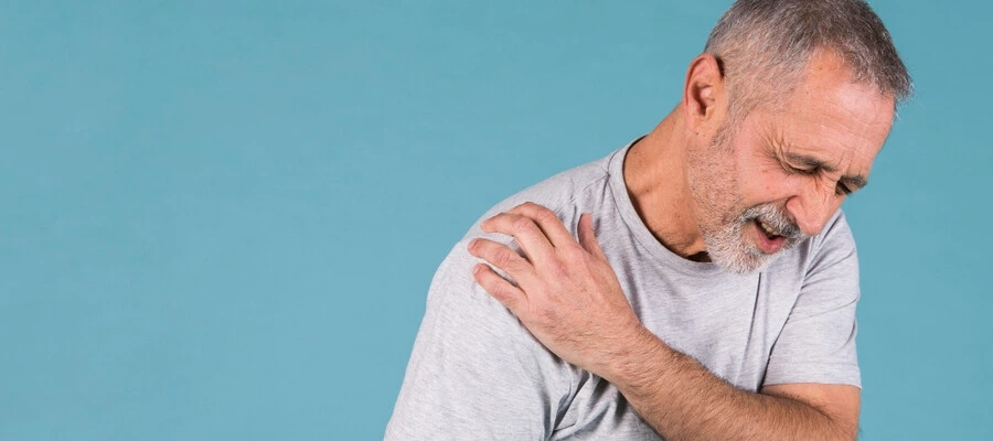 homem com camiseta cinza sentindo desconforto intenso no ombro.