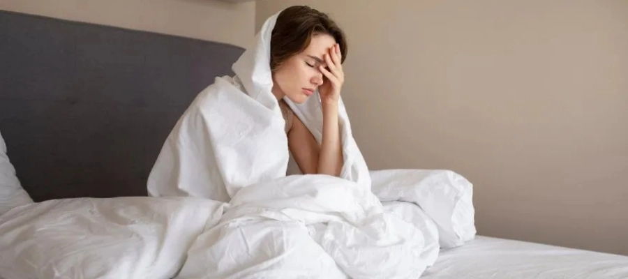 Mulher está deitada na cama e sente dor de cabeça ao acordar