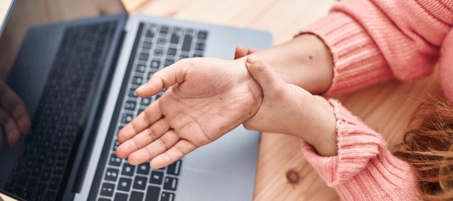 mulher trabalhando no computador segurando um dos braços com dor no punho