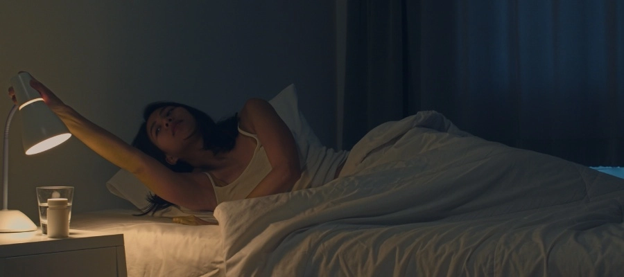 Mulher deitada na cama, diminuindo a luz do quarto para melhorar a dor de cabeça.